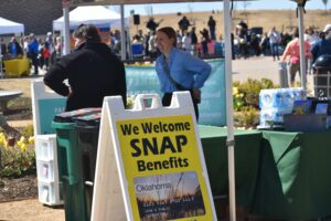 People shopping at a farmers market with a large sign that says We Welcome SNAP Benefits.