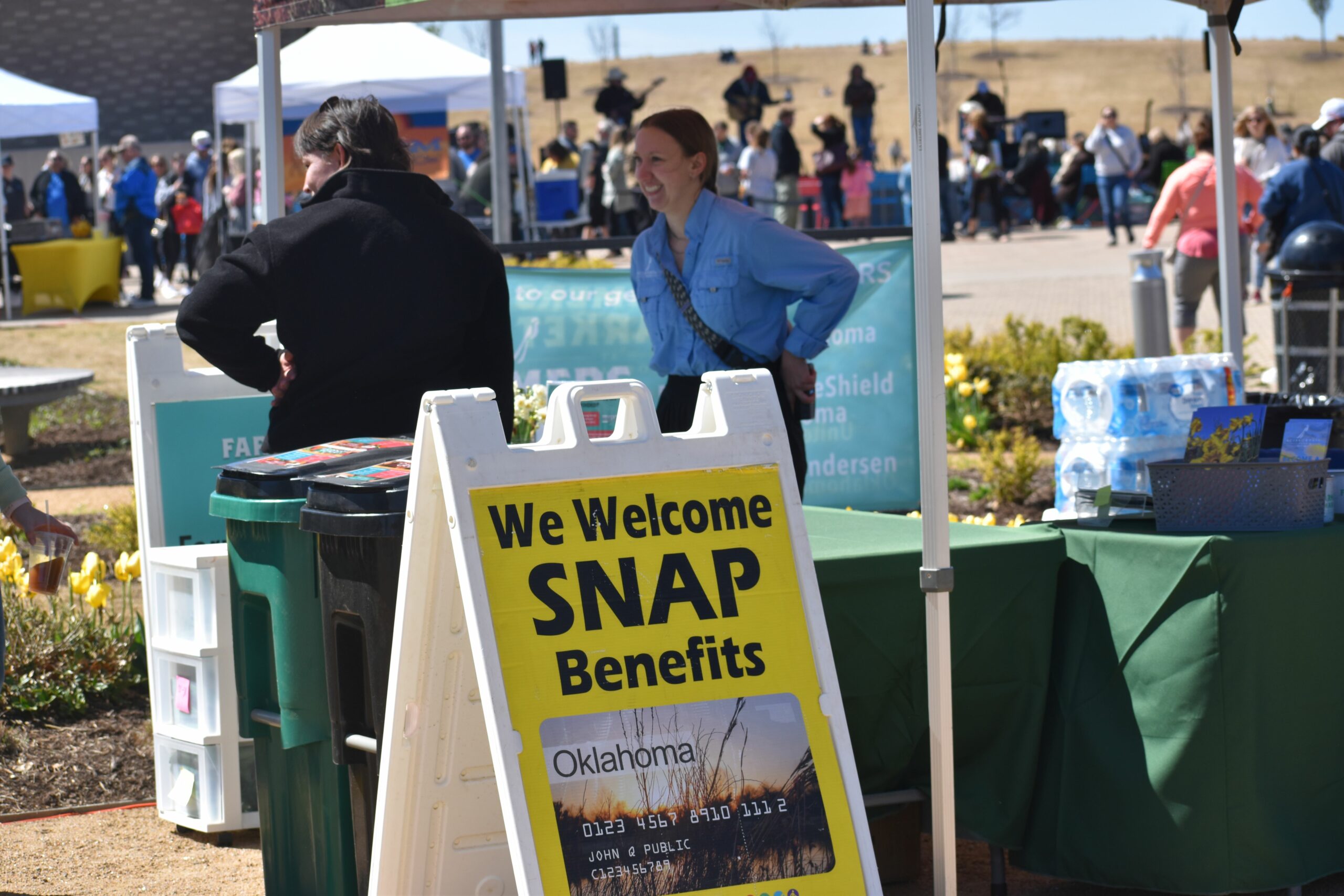 Personas comprando en un mercado de agricultores con un gran cartel que dice Damos la bienvenida a los beneficios de SNAP.