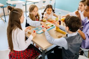 A group of diverse schoolchildren eat lunch together.